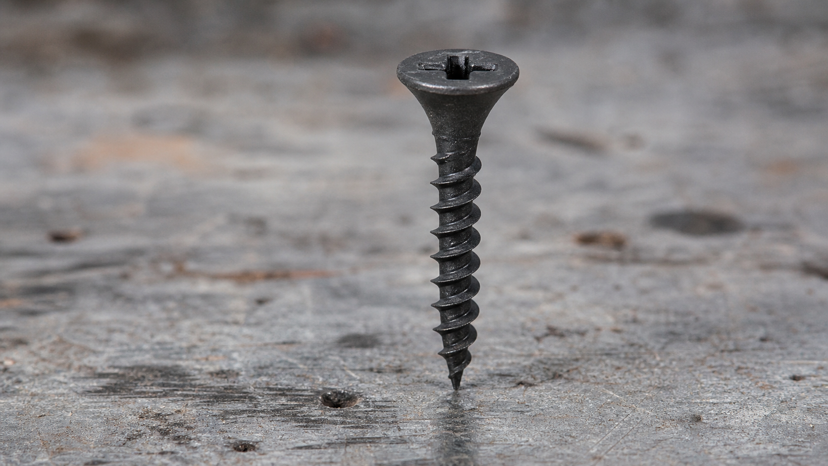 Close-up of a black phosphate drywall screw with bugle head, Phillips drive, coarse thread, and needle-point tip on a white b