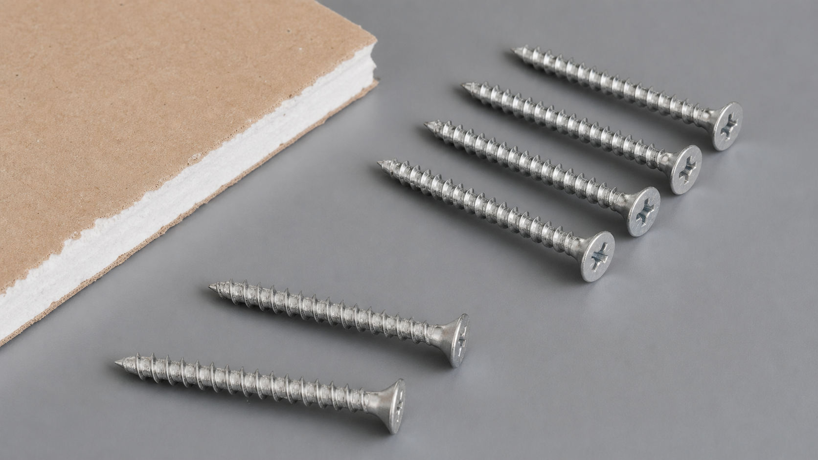Macro shot of a galvanized drywall screw bugle head with Phillips drive recess, showing countersunk shape.