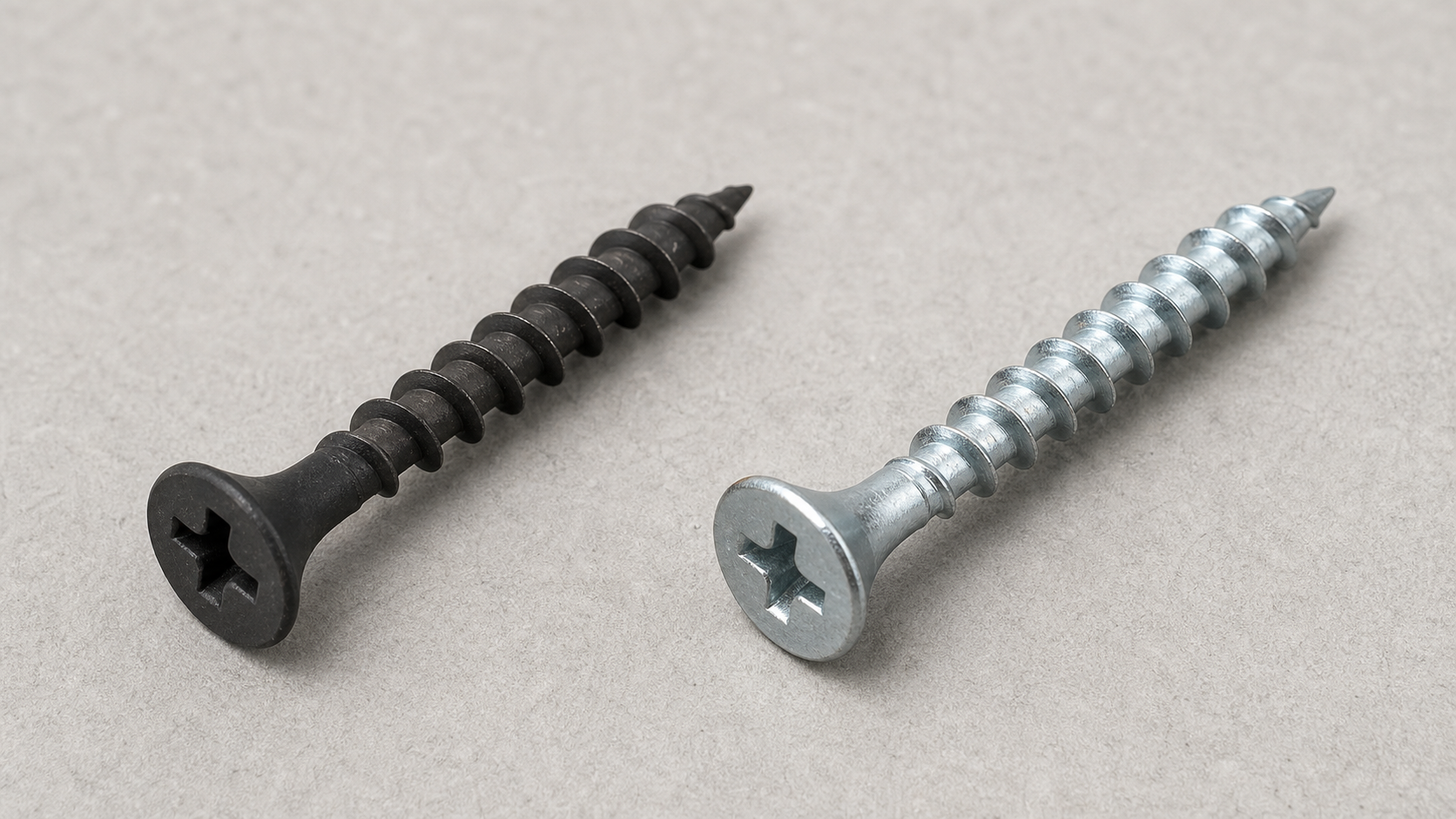Side-by-side comparison of a black phosphate drywall screw and a galvanized drywall screw on a gray surface.